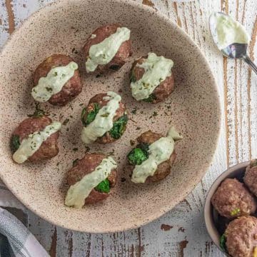 A birds eye view of air fryer turkey meatballs in a cream colored dish drizzled with creamy avocado dip.