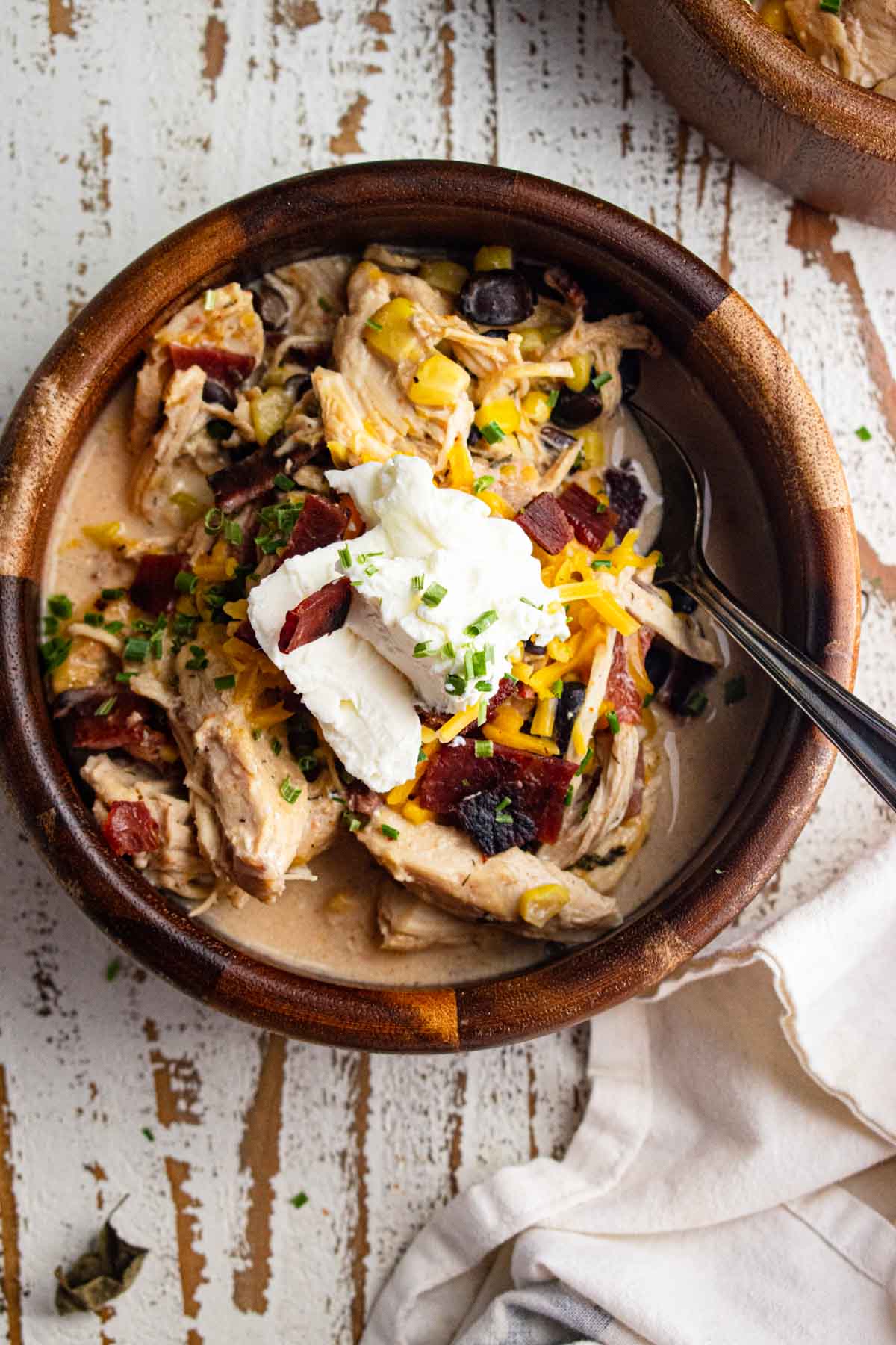 A close-up of crack chicken chili in a wooden bowl topped with plain Greek yogurt and shredded cheddar cheese.