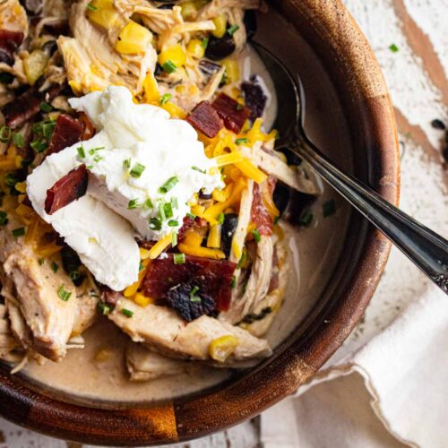 A close up of crack chicken chili in a wooden bowl with a spoon slotted into the side.