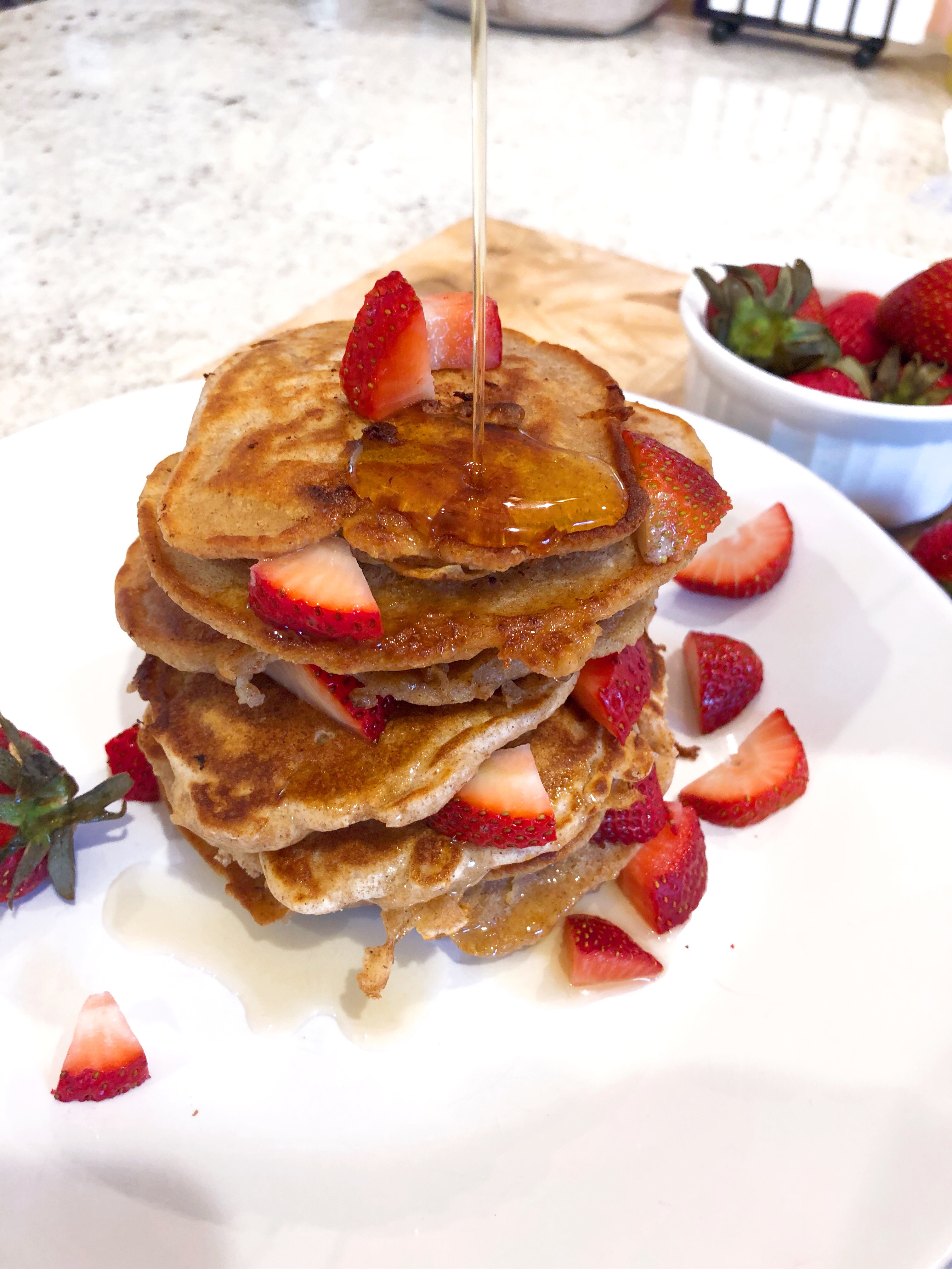 a strawberry pancakes stack being drizzles with pure maple syrup on a white plate