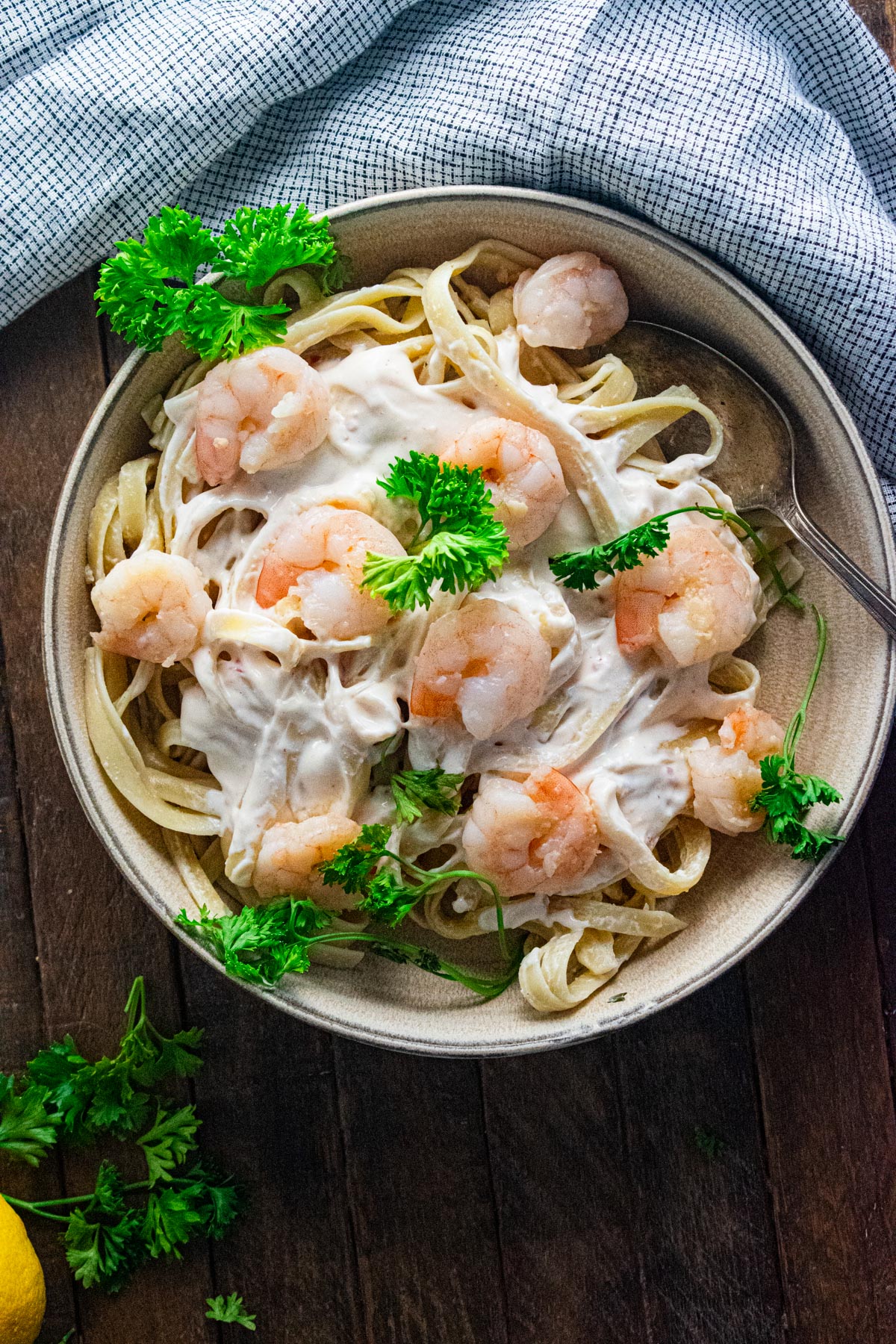 Birds eye view of bang bang shrimp in a cream colored bowl with fresh parsley scattered on top and a lemon placed next to the bowl. 