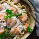A close up of bang bang shrimp pasta in a cream colored bowl with a slotted spoon in the side.