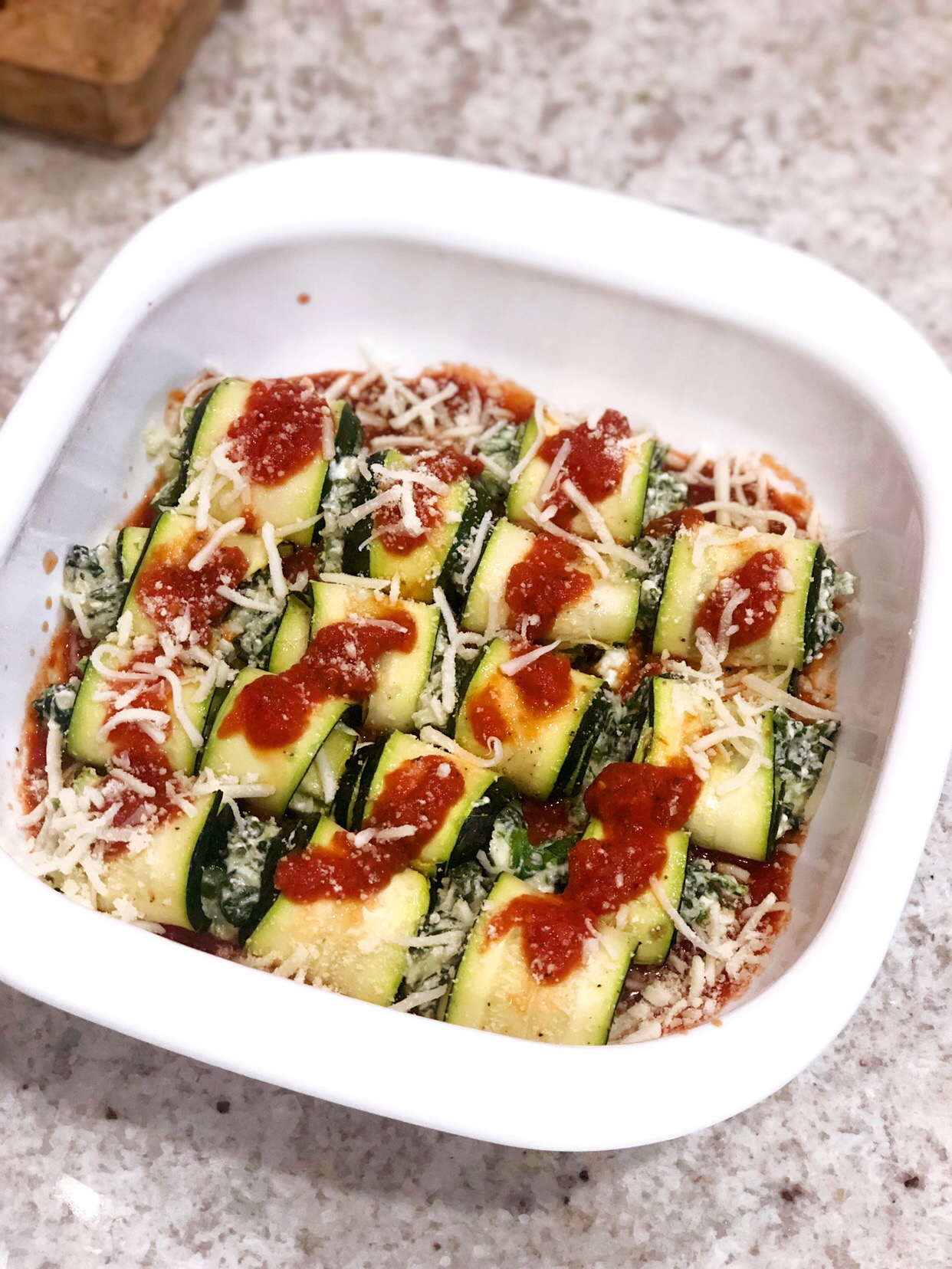zucchini roll ups in the baking dish sprinkled with cheese and marinara sauce