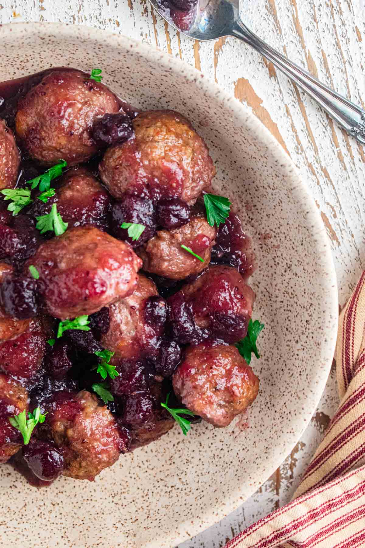 close up of juicy cranberry turkey meatballs in a cream colored bowl and topped with fresh parsley