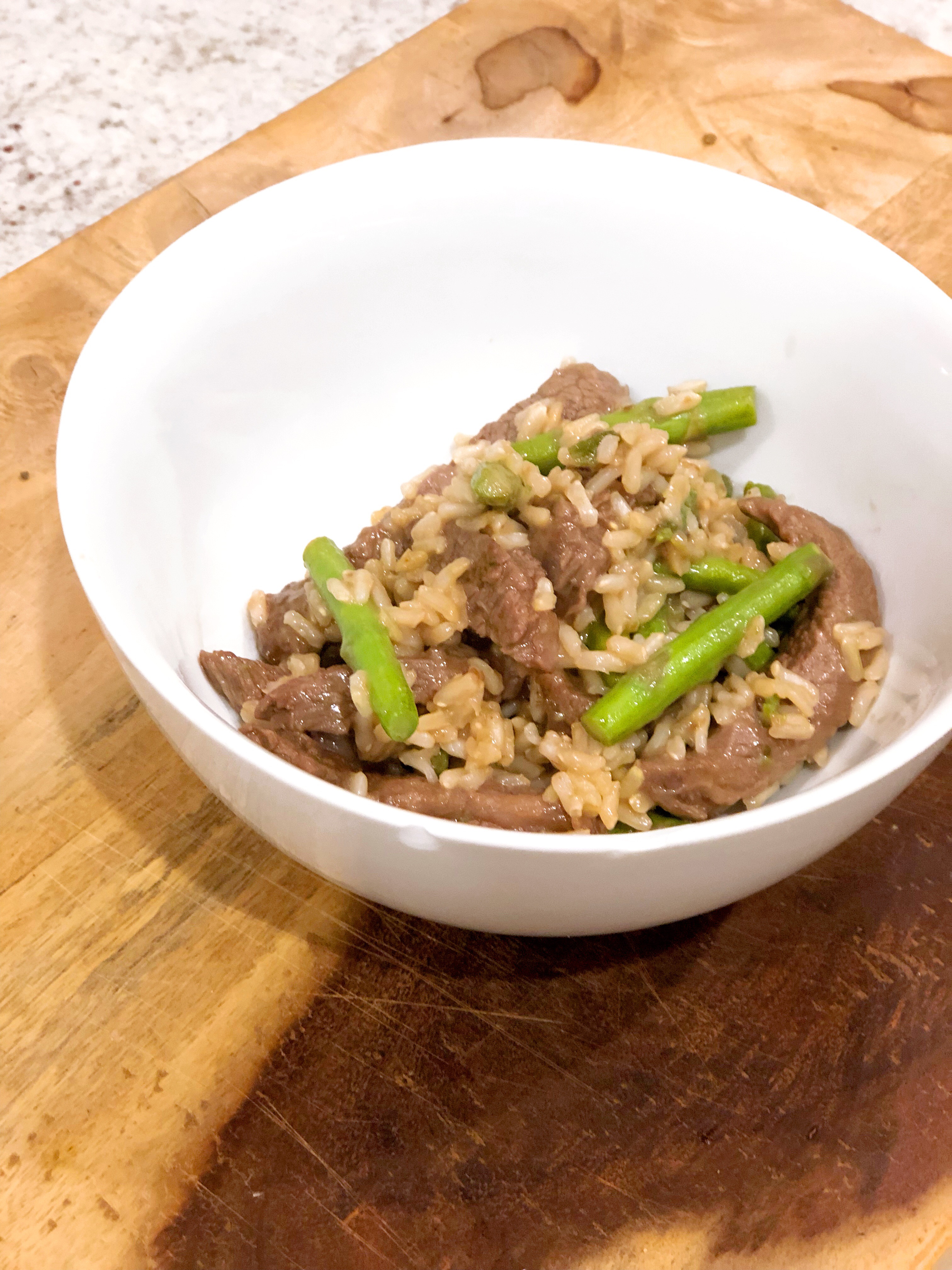 steak stir fry in a white bowl served with brown rice on a wooden cutting board