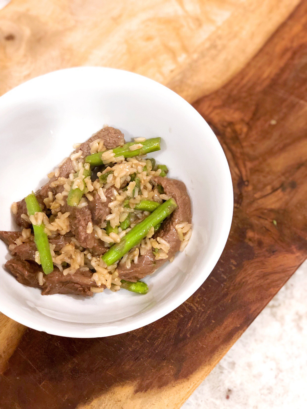 birds eye view of steak stir fry in a white bowl on a wooden cutting board