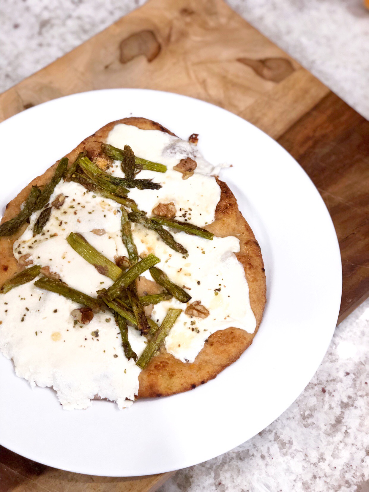 birds eye view of asparagus and naan pizza on a white plate on a wooden board