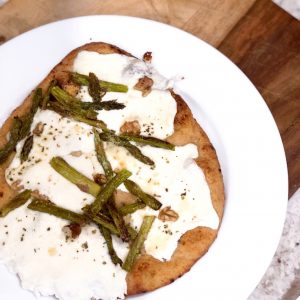 asparagus and naan pizza on a white plate on a wooden cutting board