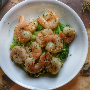 shrimp with parsley garlic butter in a white bowl over broccoli on a wooden cutting board