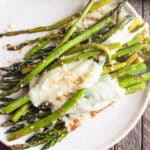Asparagus topped with melted cheese on a white plate.