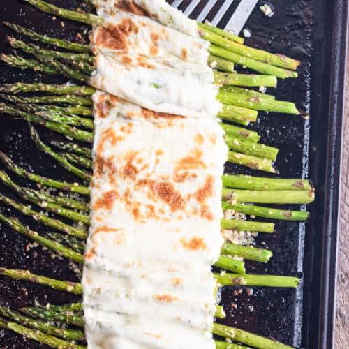 Asparagus lined on a baking sheet topped with melted cheese.