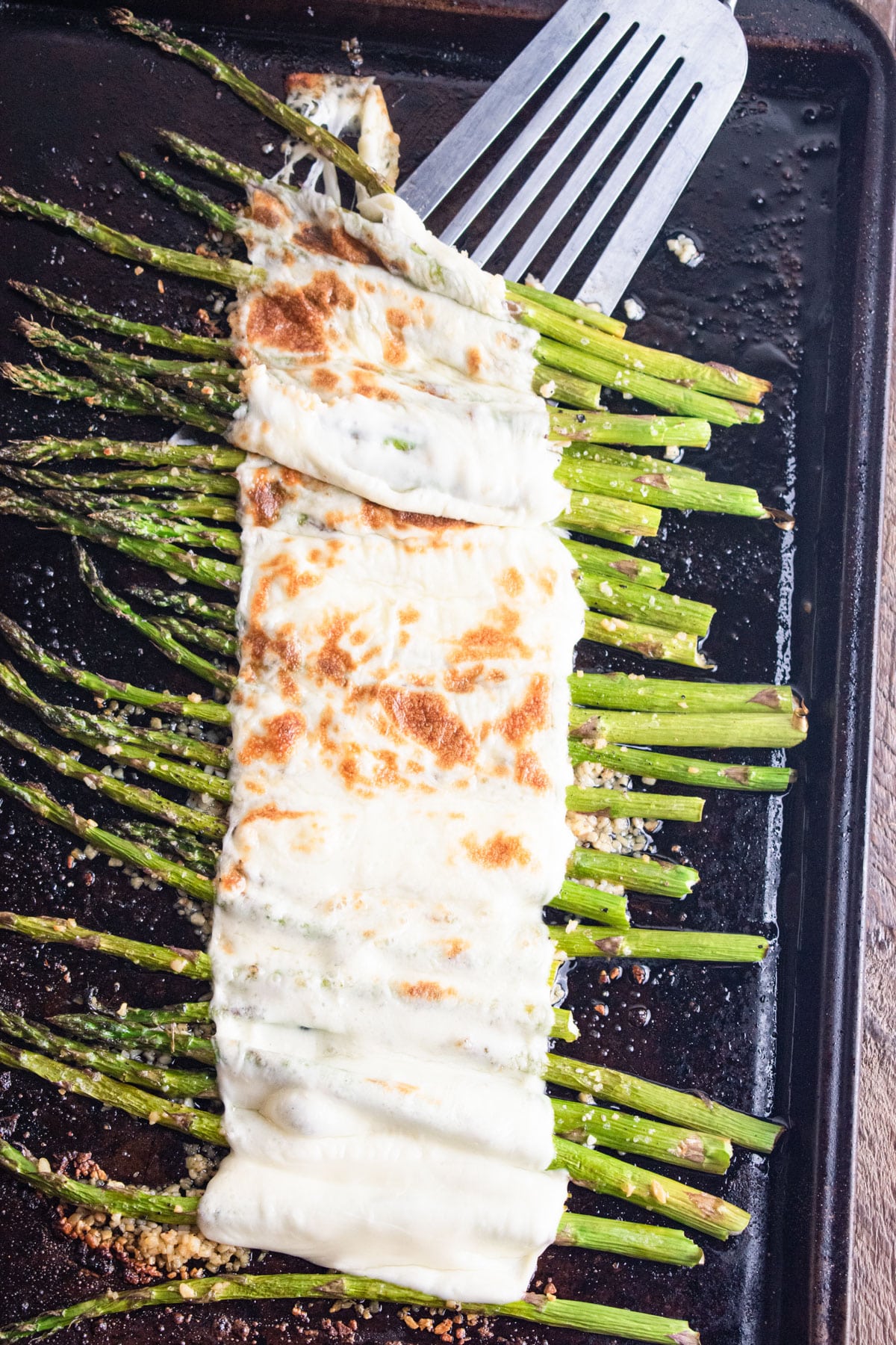 Asparagus lined on a baking sheet topped with melted cheese.