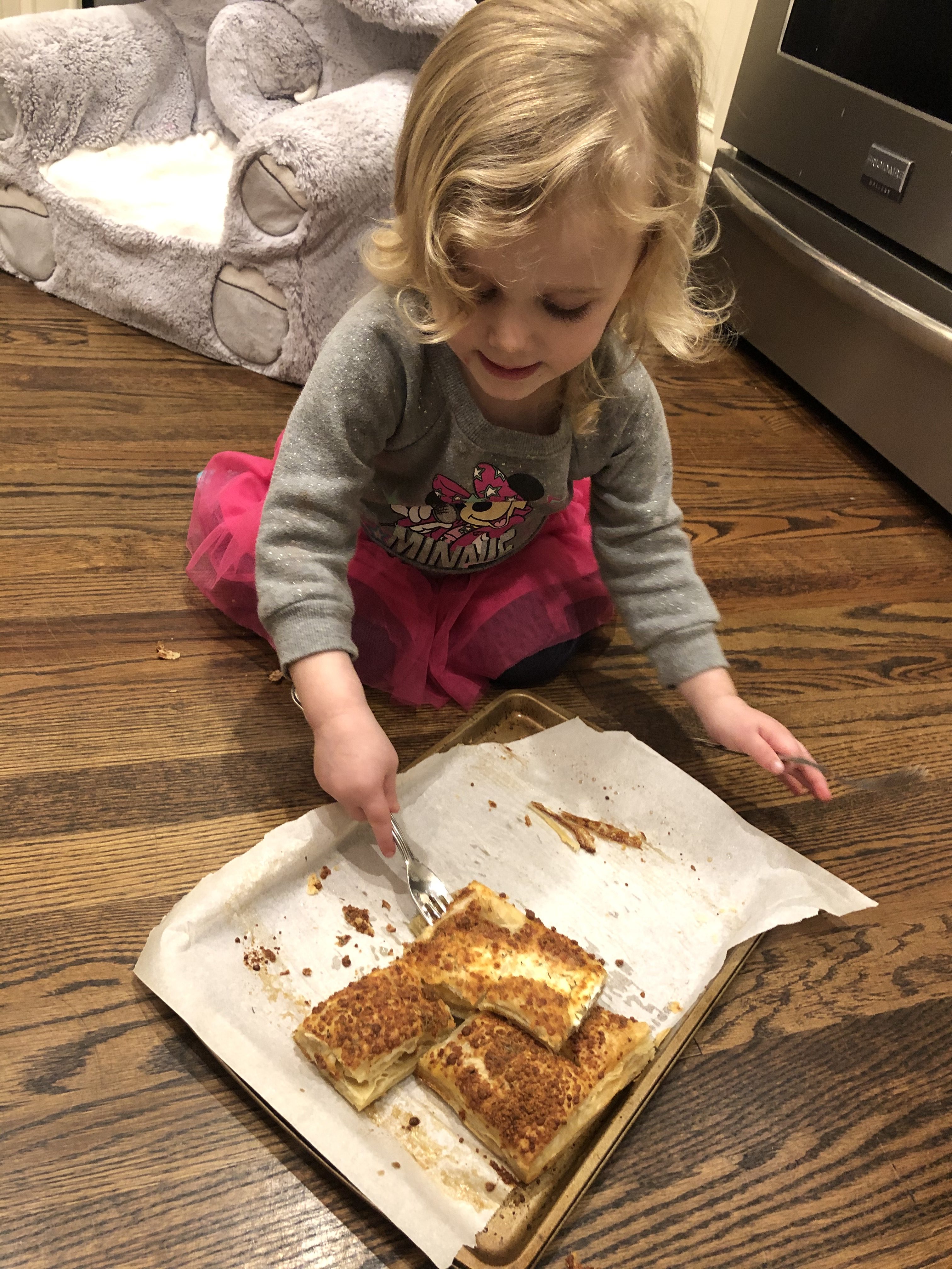 Little girl with blonde hair cutting cheese crisps in pieces