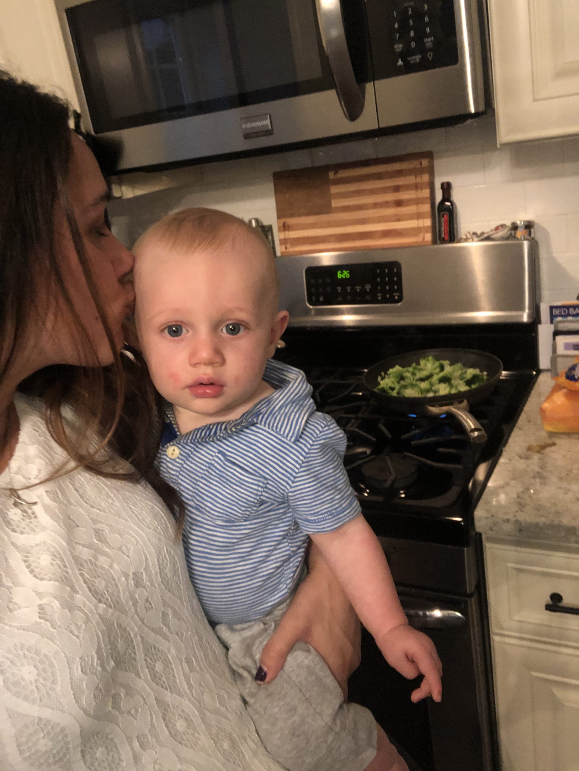 Woman in white shirt holding baby next to cooking broccoli