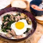 fried egg served over sausage and spinach in a maroon bowl