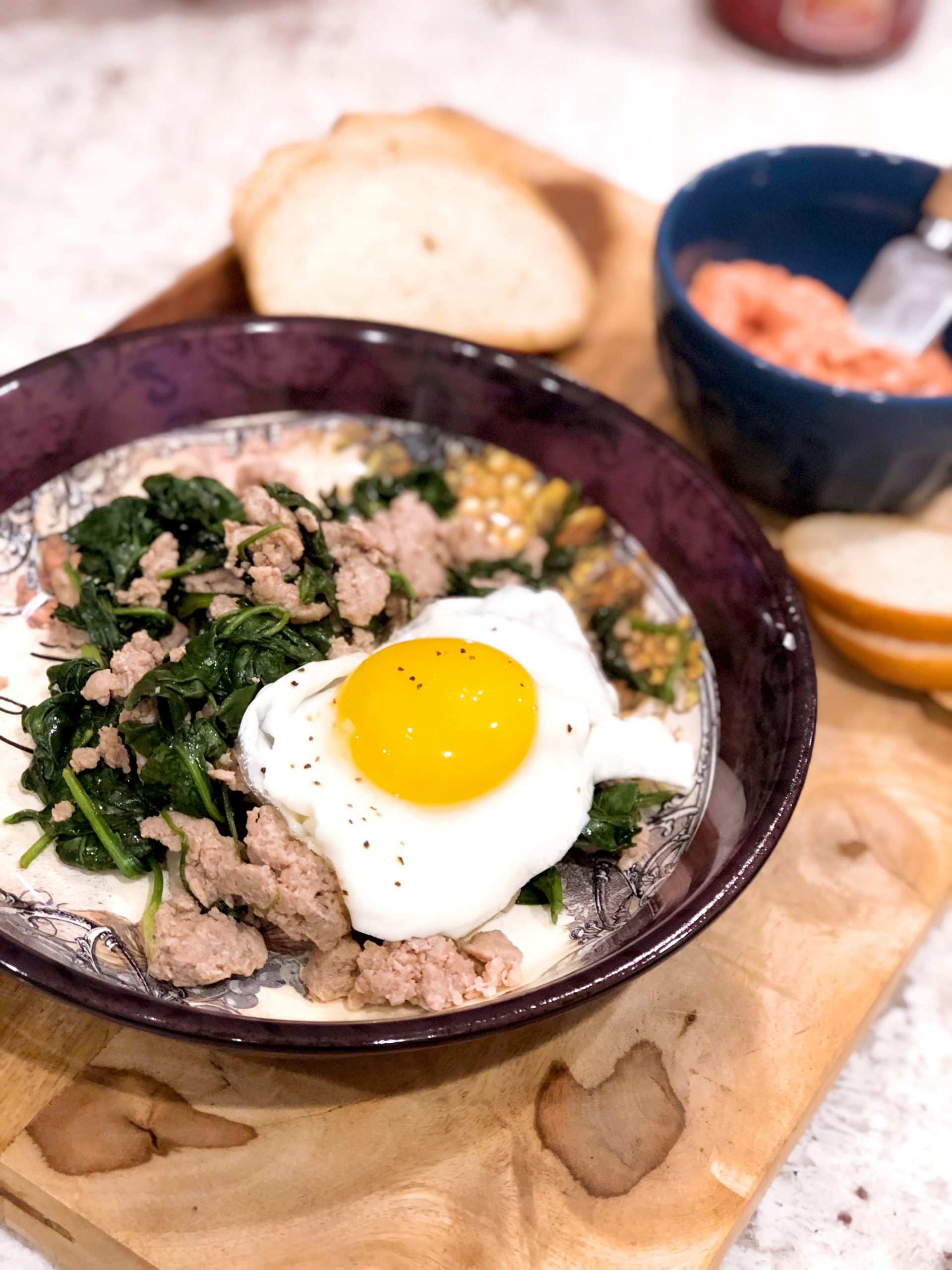 fried egg served over sausage and spinach in a maroon bowl