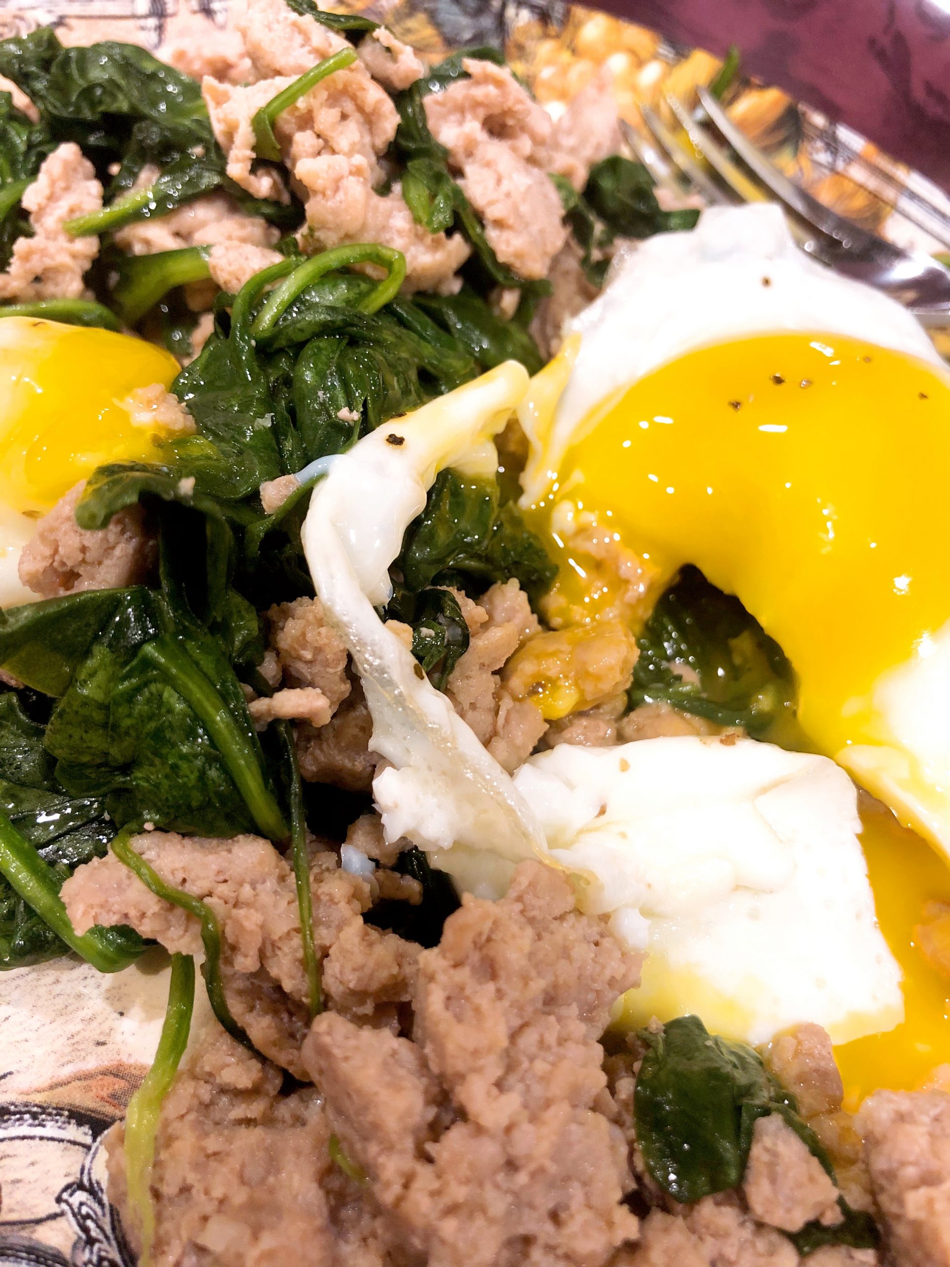 Fried egg drizzling over turkey sausage and spinach