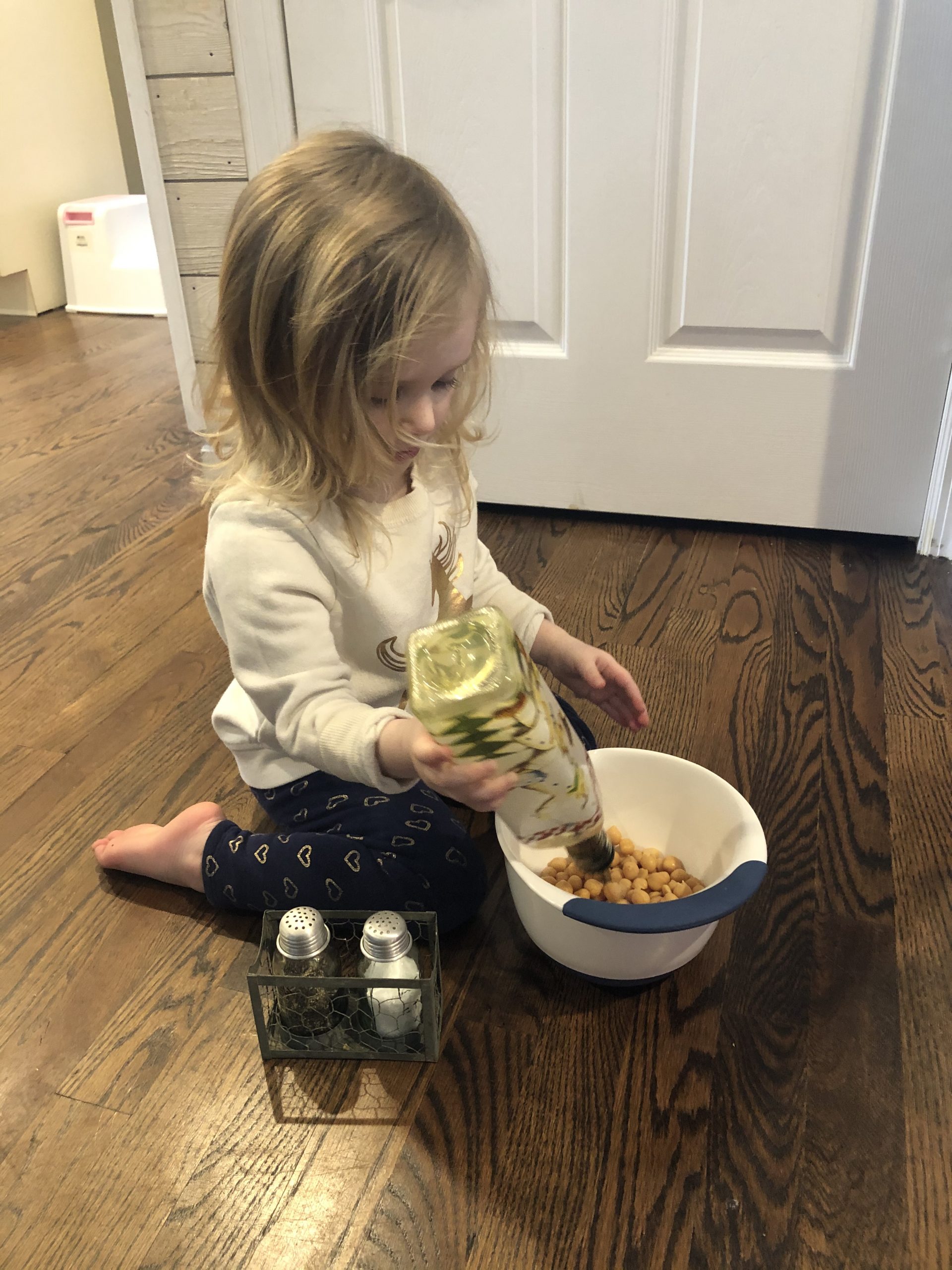 little girl pouring oil into a bowl of chickpeas