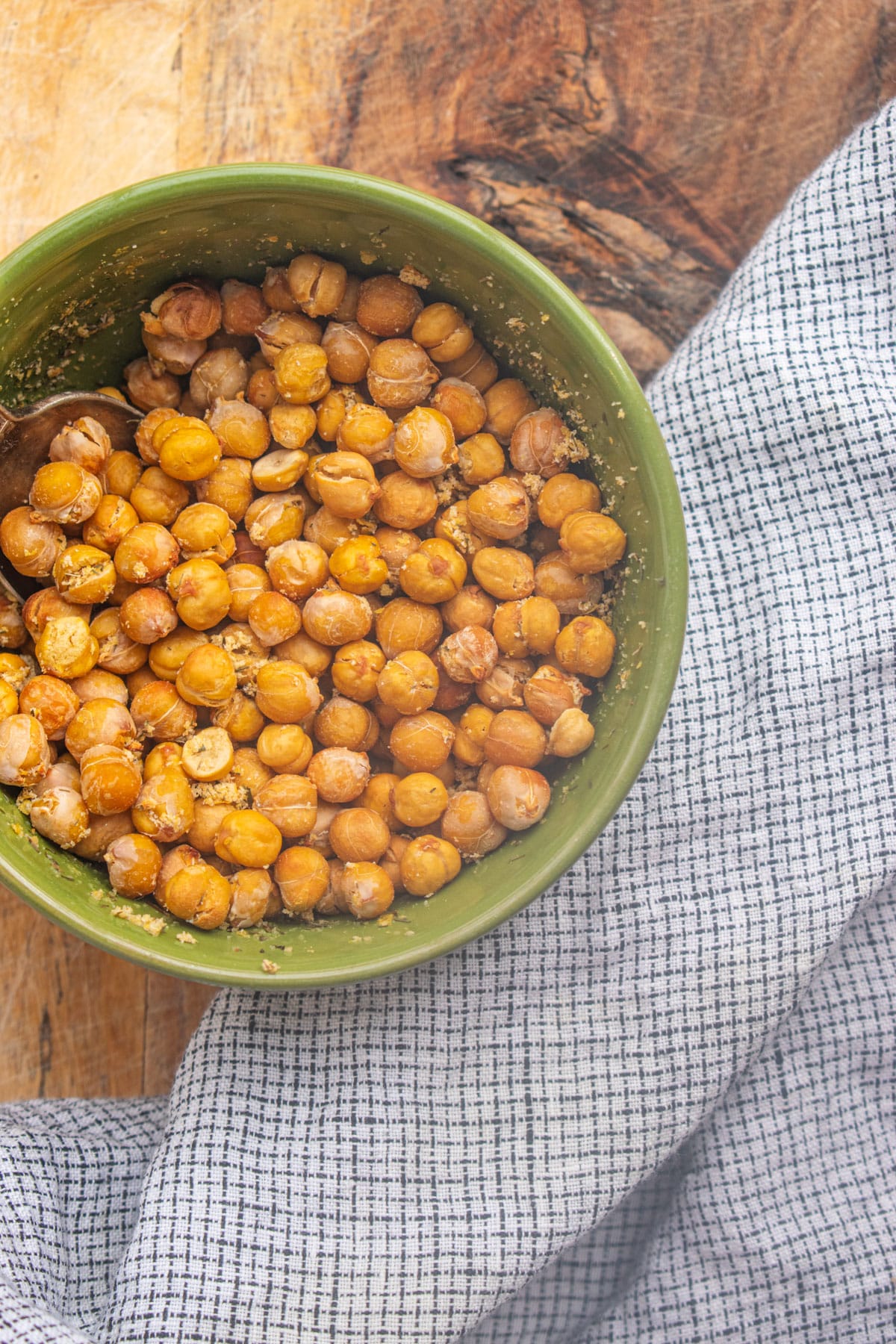 Birds eye view of roasted chickpeas in a green bowl on a wooden table.
