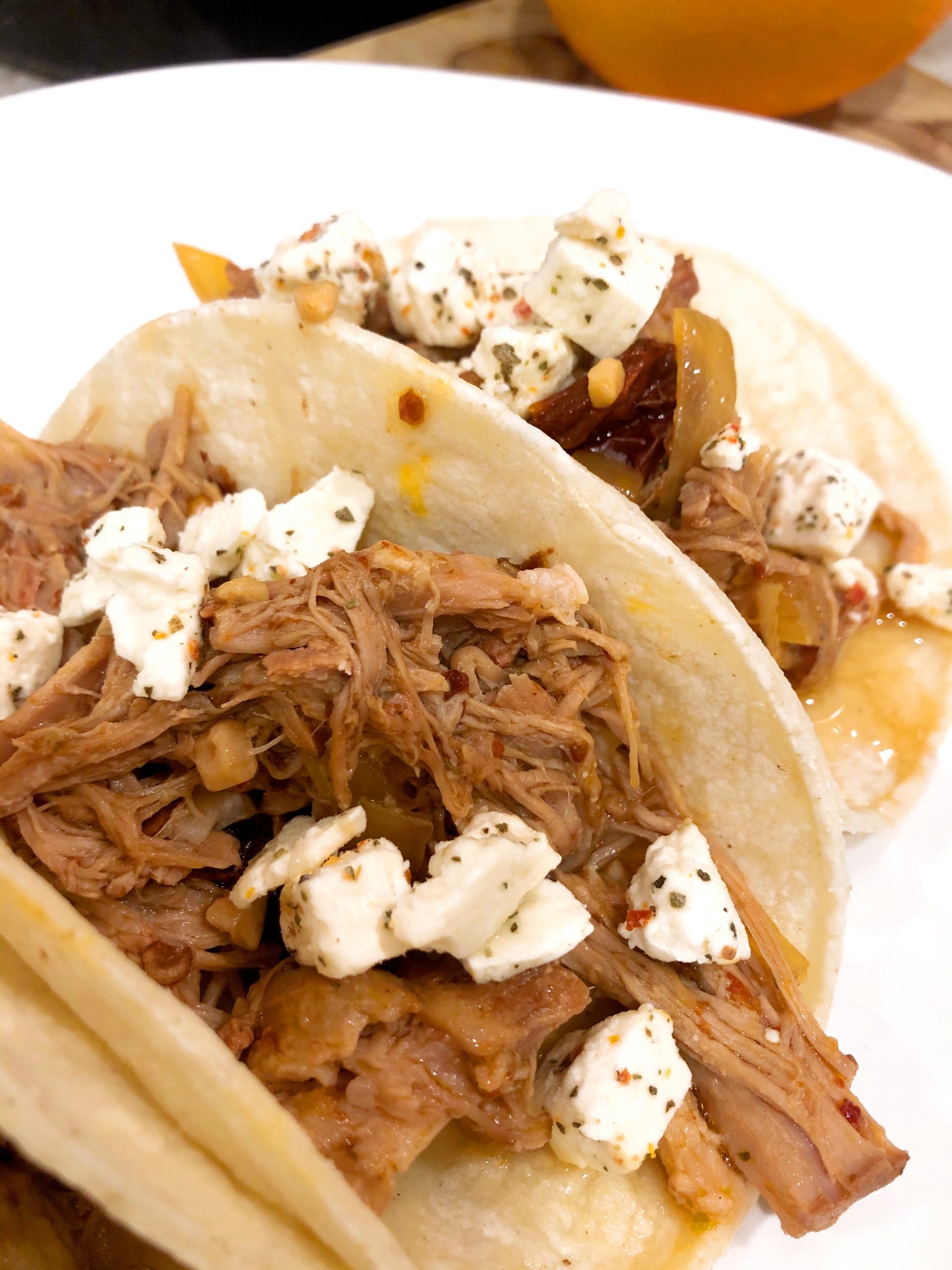 close up of pulled pork tacos on corn tortillas topped with feta cheese