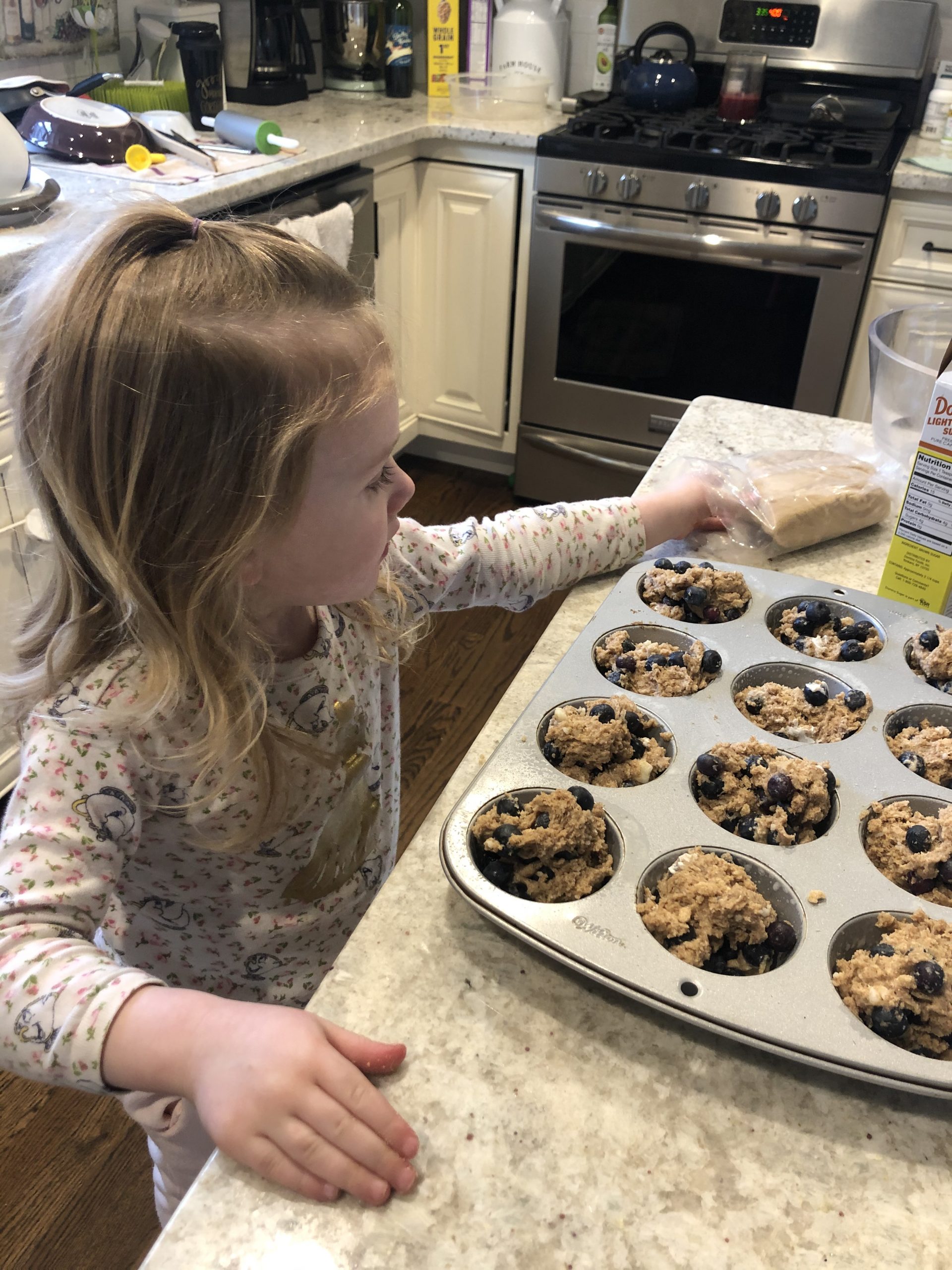 little girl sprinkling light brown sugar on top of the healthy blueberry muffins