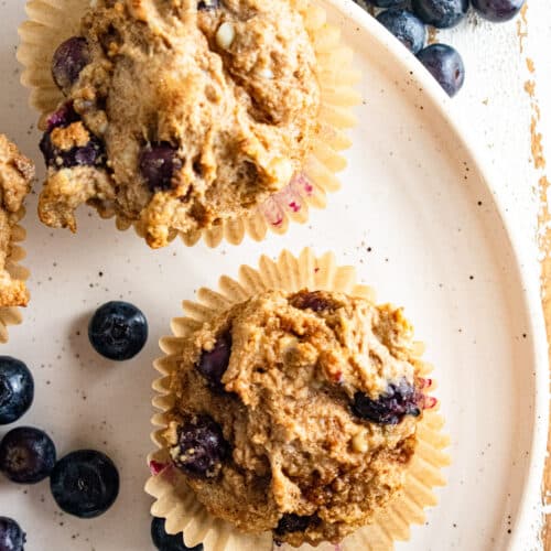 A close up of healthy cottage cheese blueberry muffins on a white plate with blueberries scattered around.