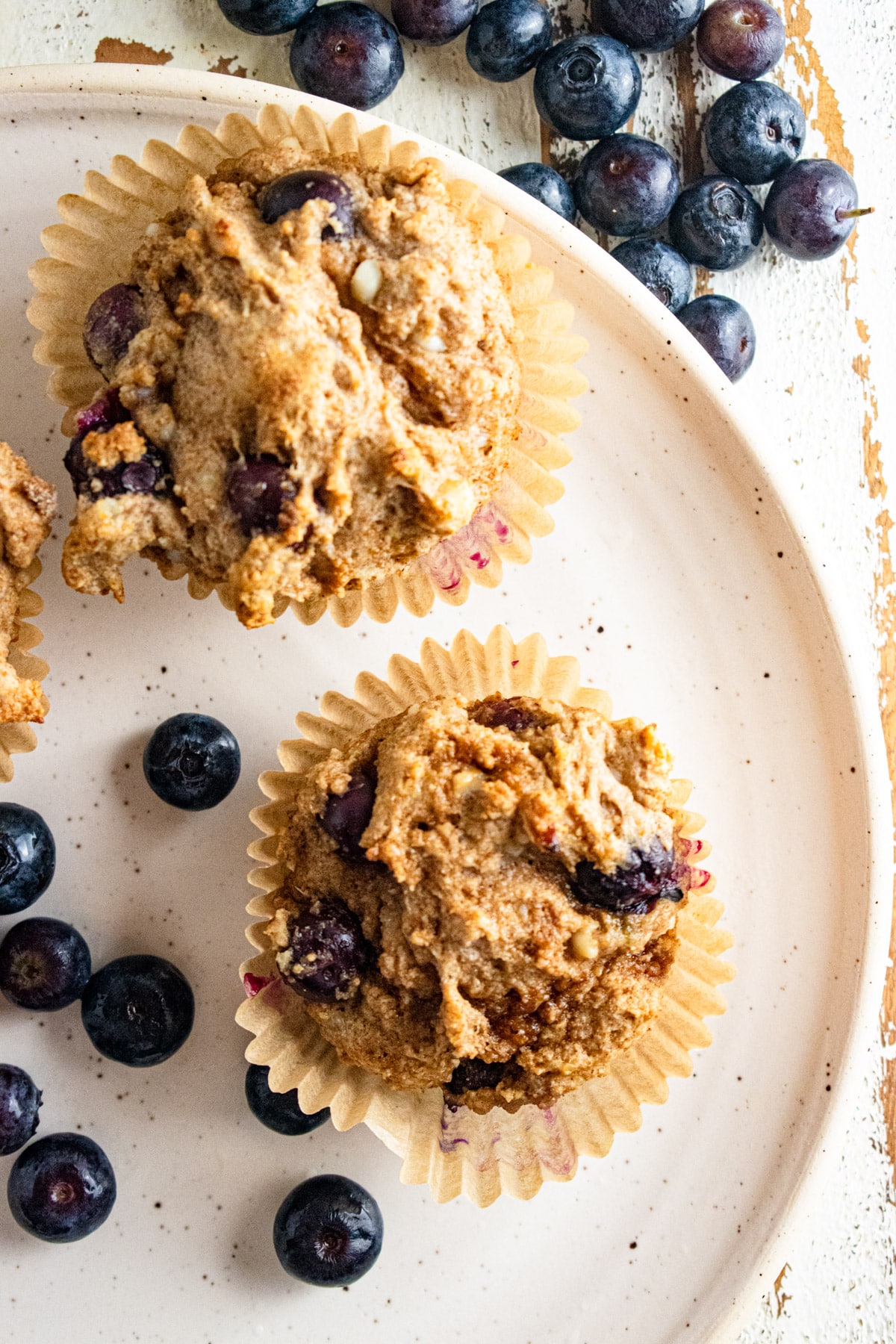 A close up of healthy cottage cheese blueberry muffins on a white plate with blueberries scattered around.