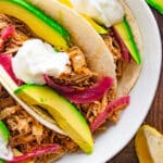 Close up of pulled pork tacos in hard taco shells in a white bowl on a wooden table.
