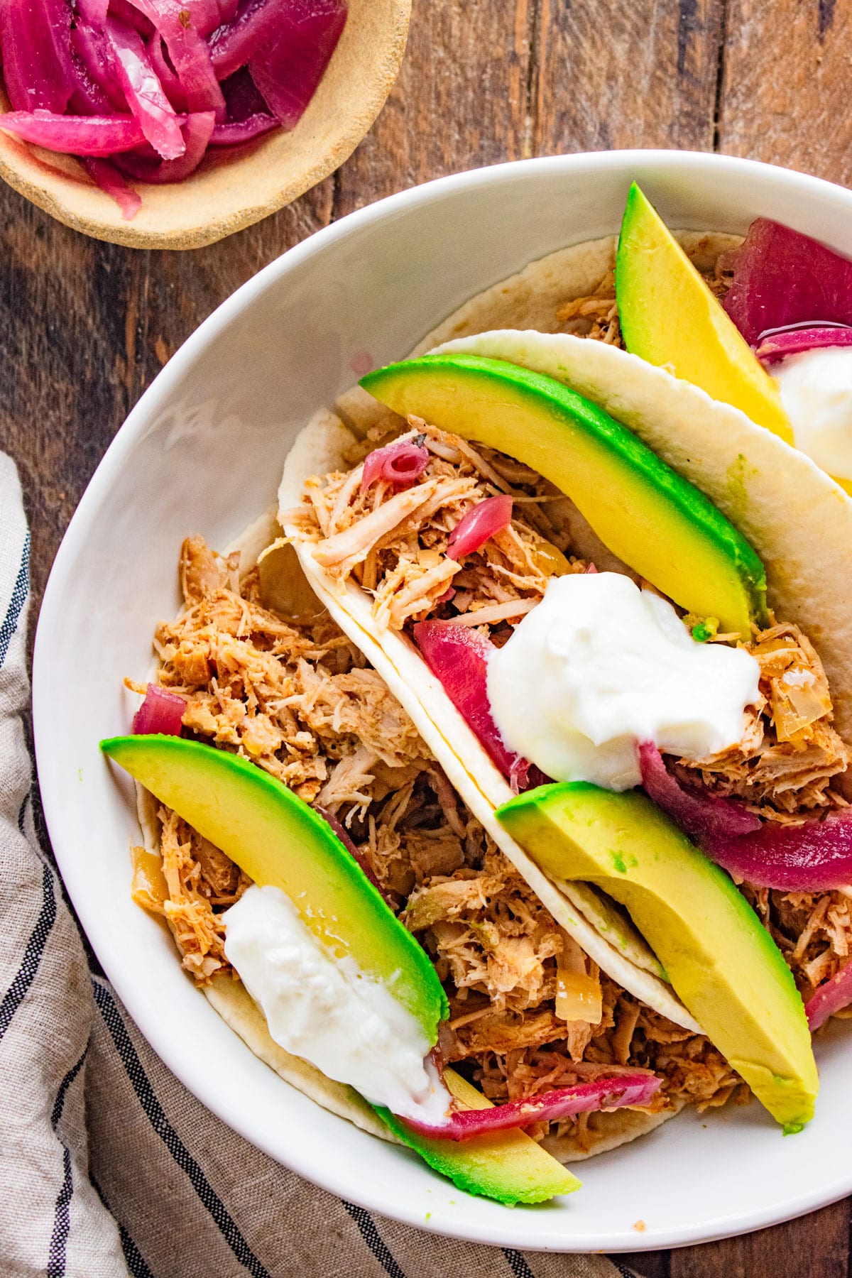 Close up of pulled pork tacos in hard taco shells in a white dish on a wooden table.