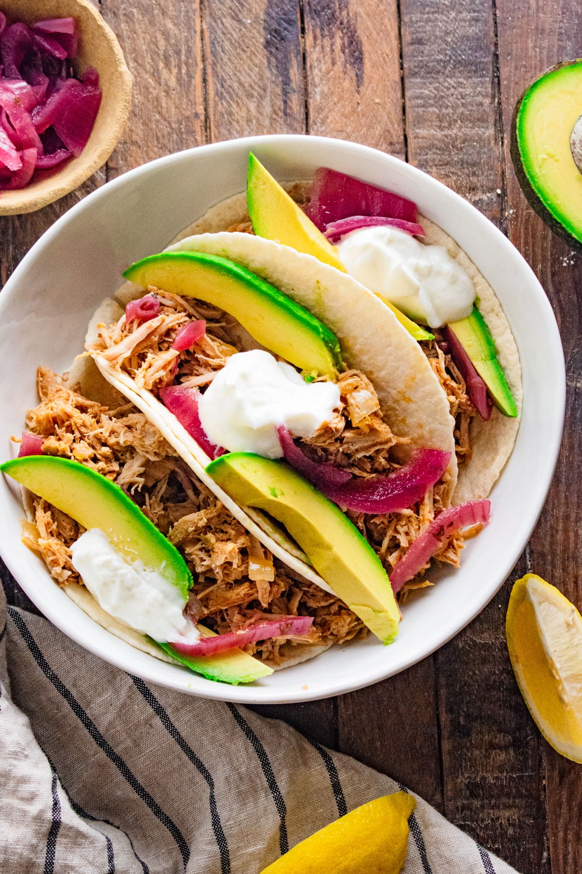 Birds eye view of pulled pork tacos in taco shells in a white dish on a wooden table.
