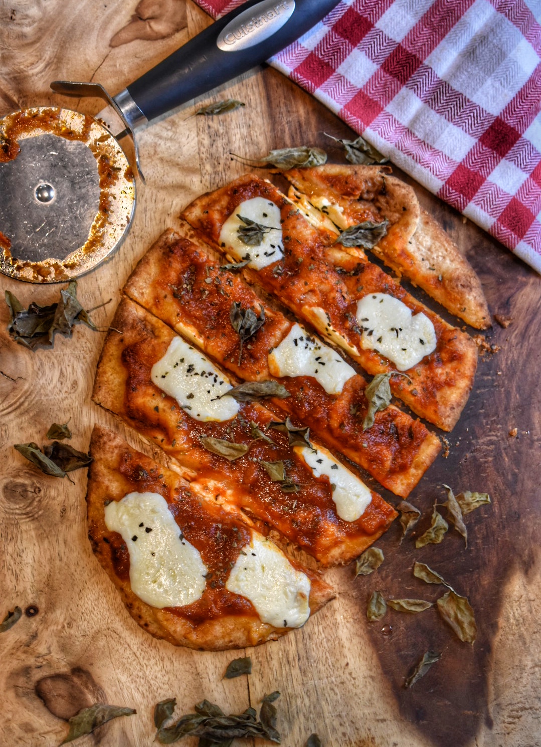 birds eye view of naan basic naan pizza on a cutting board with a pizza cutter and checkered table cloth