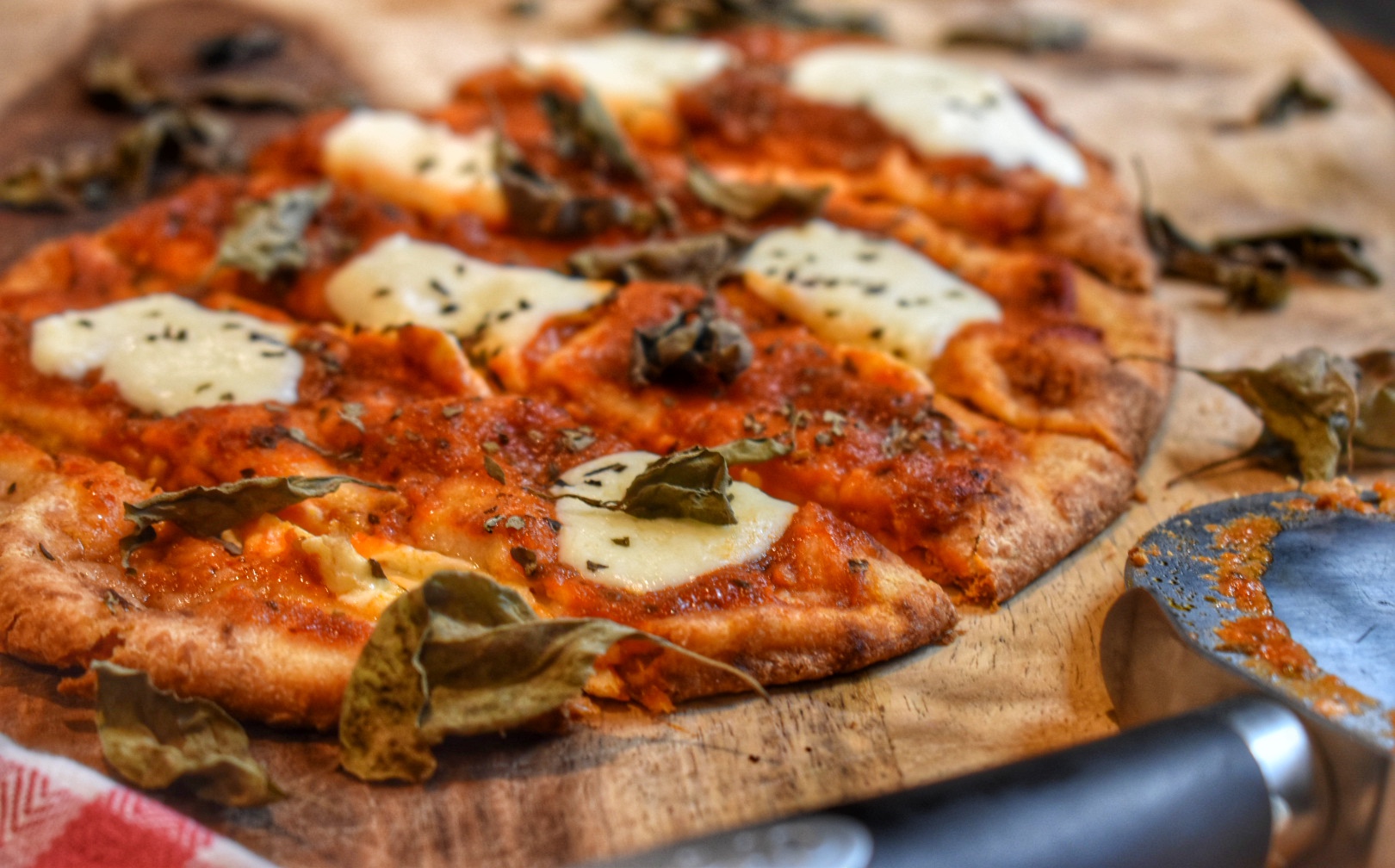 close up of naan pizza on a cutting board with tomato sauce and melted mozzarella topped with basil