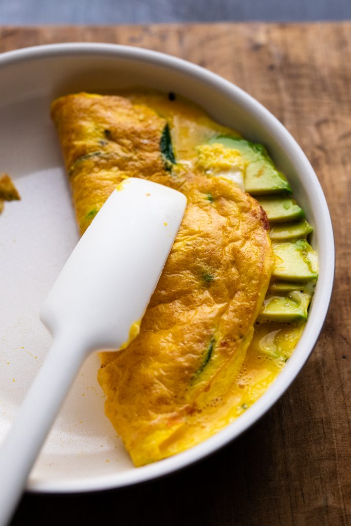 A white rubber spatula flipping an omelette in a pan.