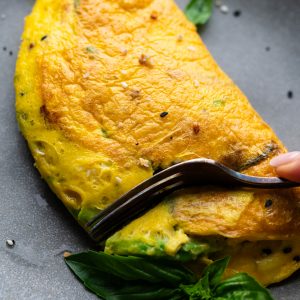 A fork cutting into an avocado omelette that's sitting on a gray plate.