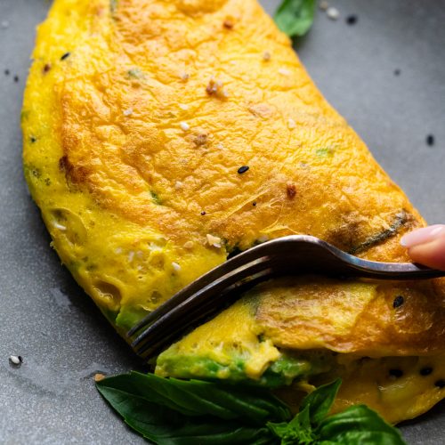 A fork cutting into an avocado omelette that's sitting on a gray plate.