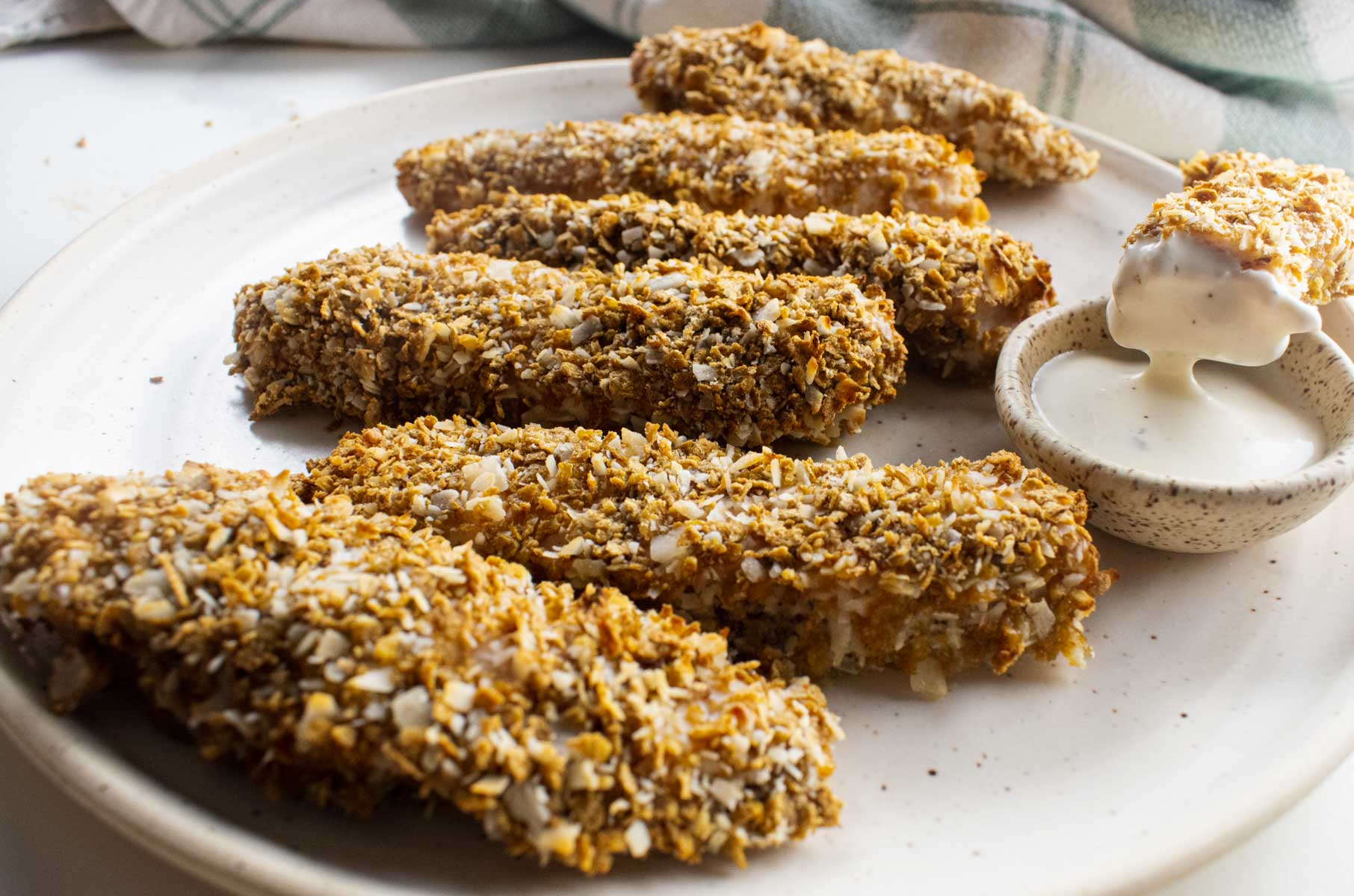 close up of coconut crusted on a white plate with a dipping sauce