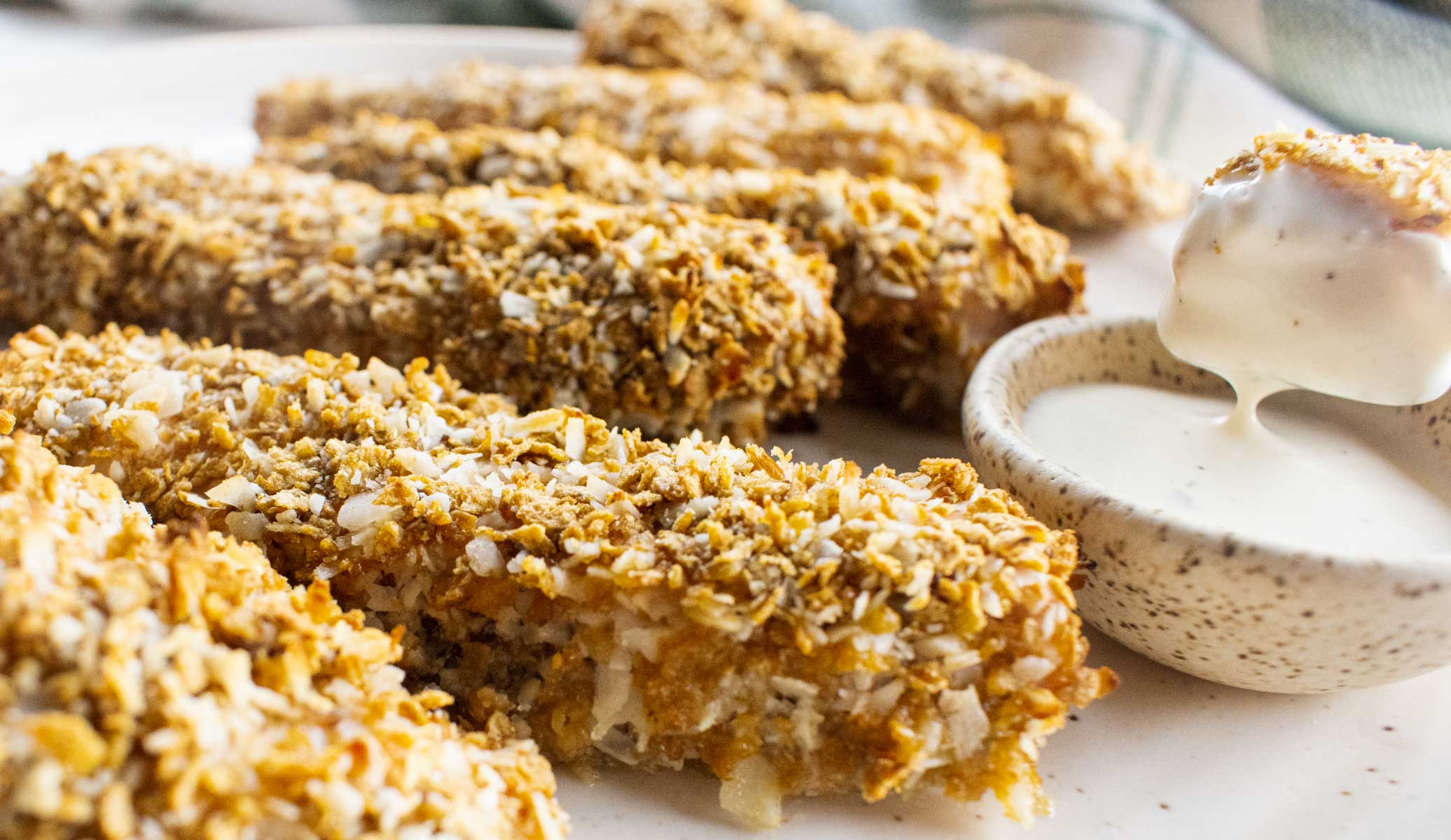 close up of coconut crusted chicken strips with a dipping sauce