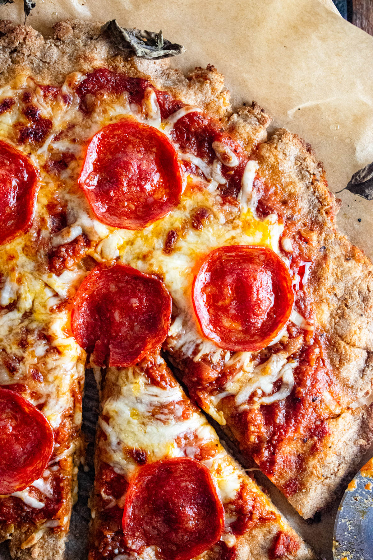 Close up of cottage cheese pizza crust topped with sauce cheese and pepperoni on a piece of parchment paper.