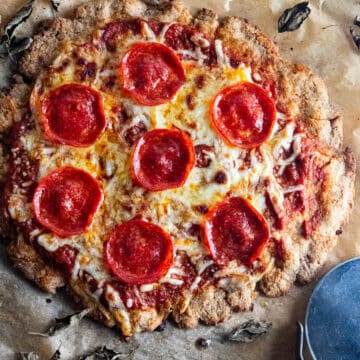 Cottage chees pizza crust on a piece of parchment paper with a pizza cutter laid next to it.