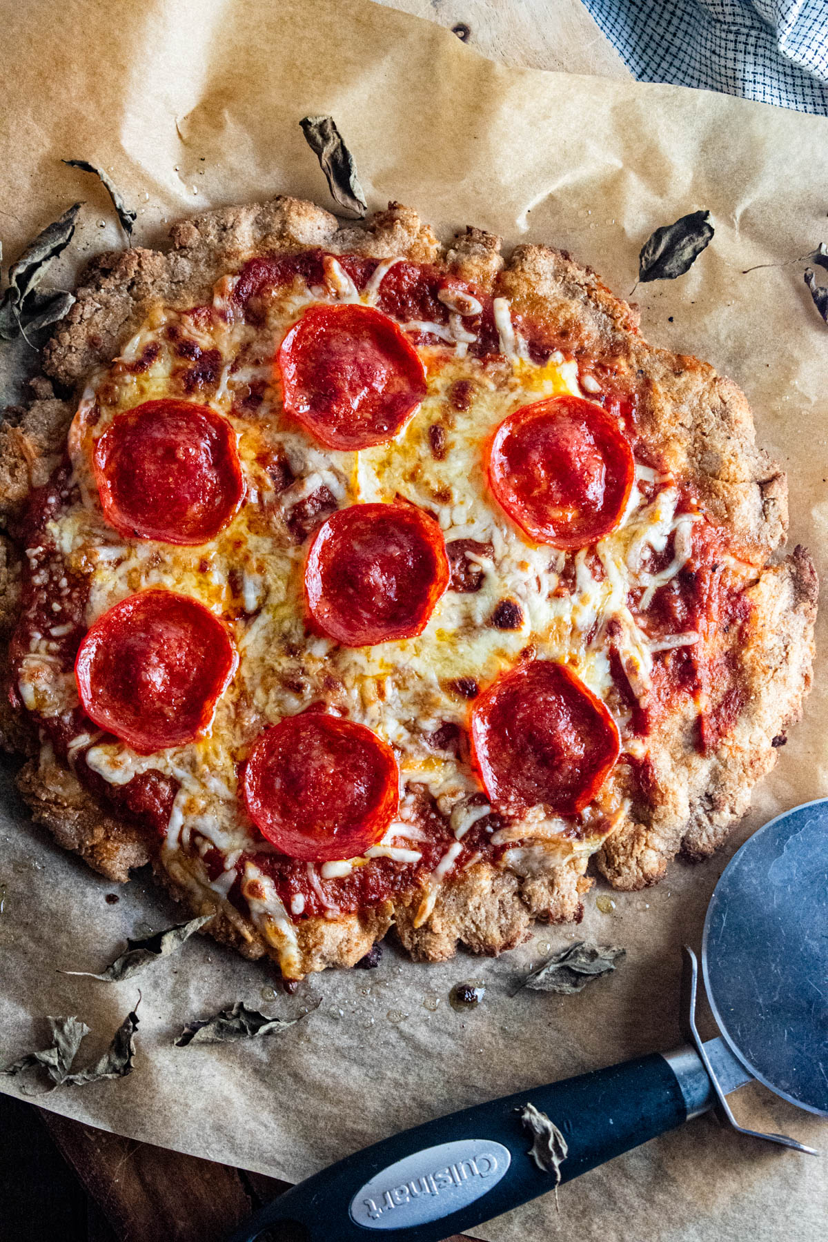 Cottage chees pizza crust on a piece of parchment paper with a pizza cutter laid next to it.