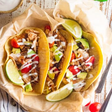 Mahi Mahi fish tacos in a cream colored dish with 3 limes on top and cherry tomatoes scattered to the side.