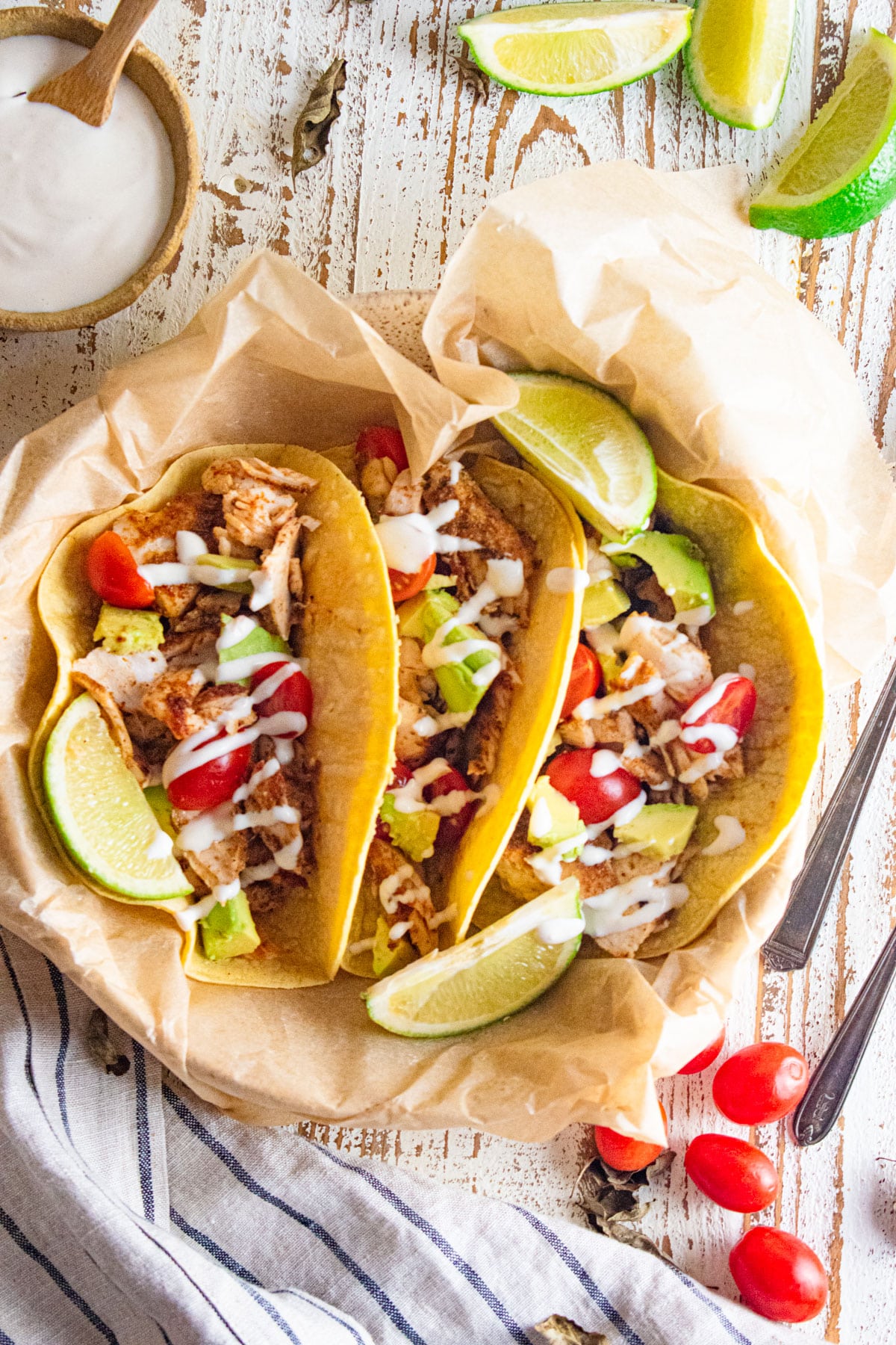 Mahi Mahi fish tacos in a cream colored dish with 3 limes on top and cherry tomatoes scattered to the side.