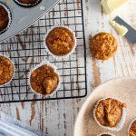 Flourless pumpkin oatmeal muffins on a cooling rack and in a muffin tin on a white wooden table.