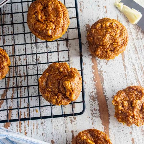 pumpkin flourless oatmeal muffins on a wire baking rack and some on a white wooden table.