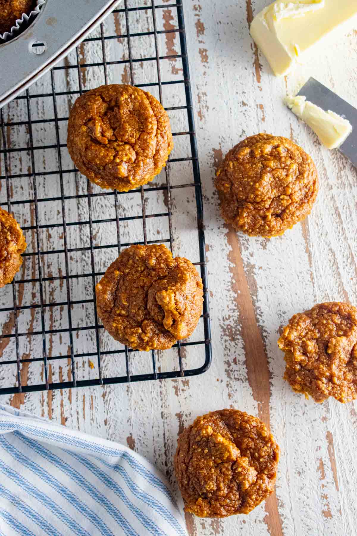 pumpkin flourless oatmeal muffins on a wire baking rack and some on a white wooden table.