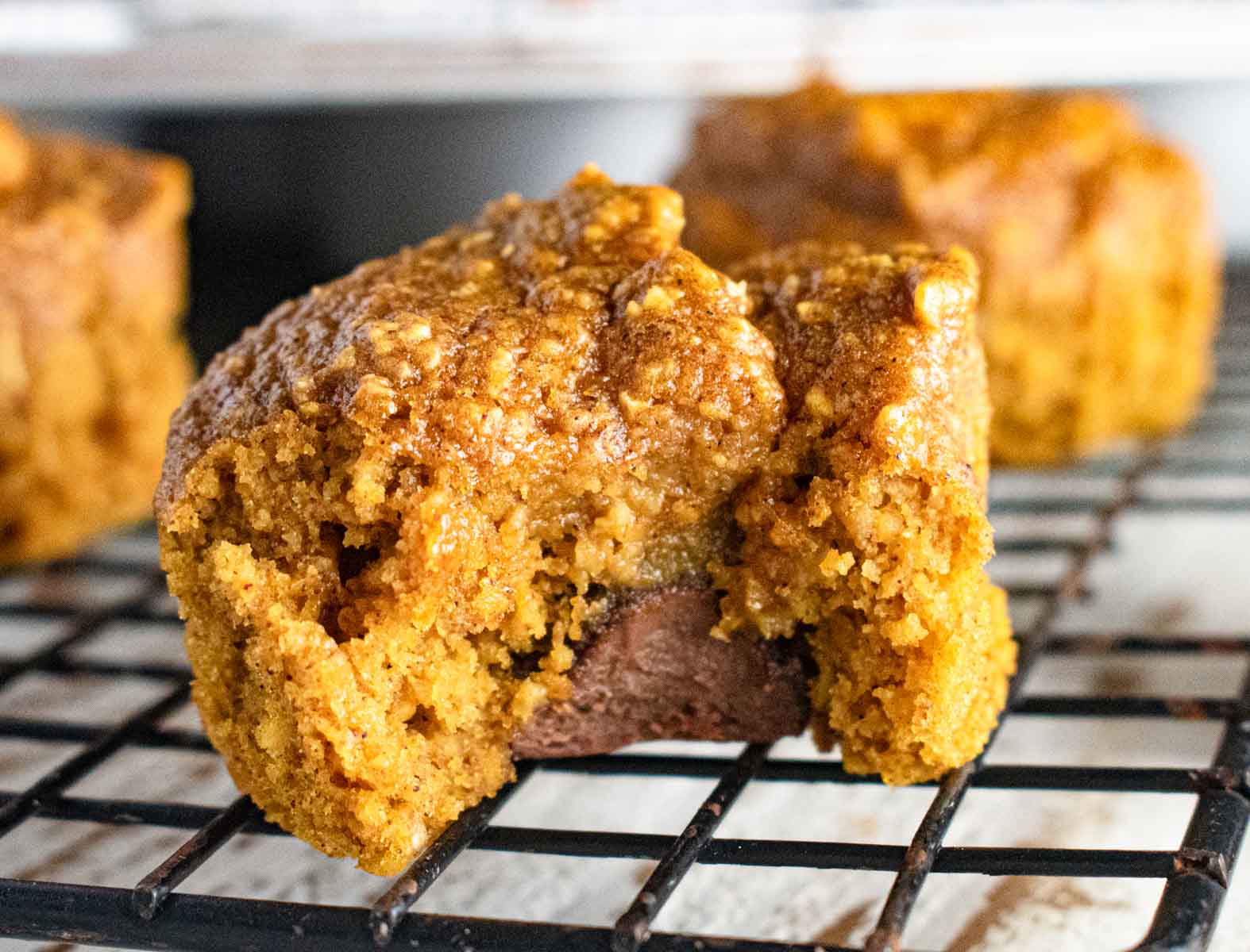 close up of the flourless oatmeal pumpkin muffins on a cooling rack with a bite taken out showing a Hershey's kiss inside the muffin.