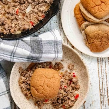 Birds-eye view of a healthy sloppy joe on a white plate with a cast iron skillet filled with sloppy joe mix next to a plate of whole wheat buns.