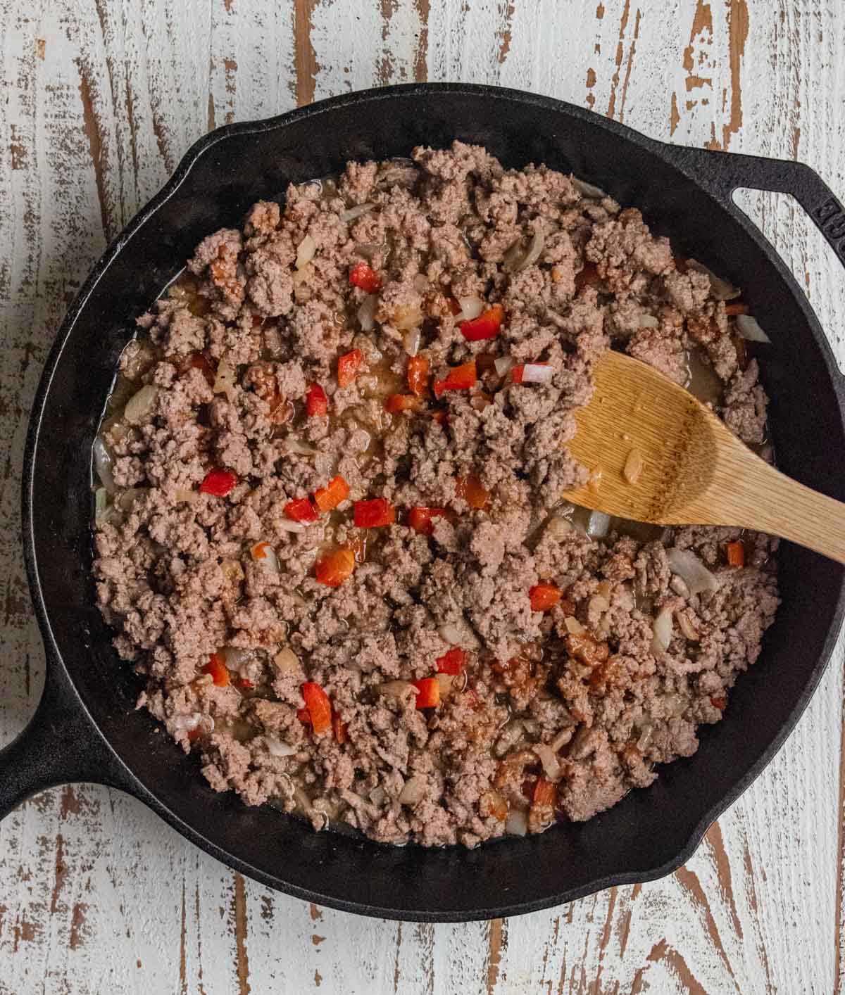 Step 2 - Ground turkey, red bell peppers, and onions cooking in a cast iron skillet with a slotted wooden spoon