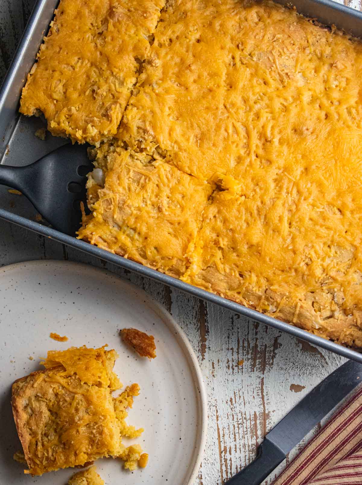 close up of scalloped corn on a white plate next to a casserole in a tin dish