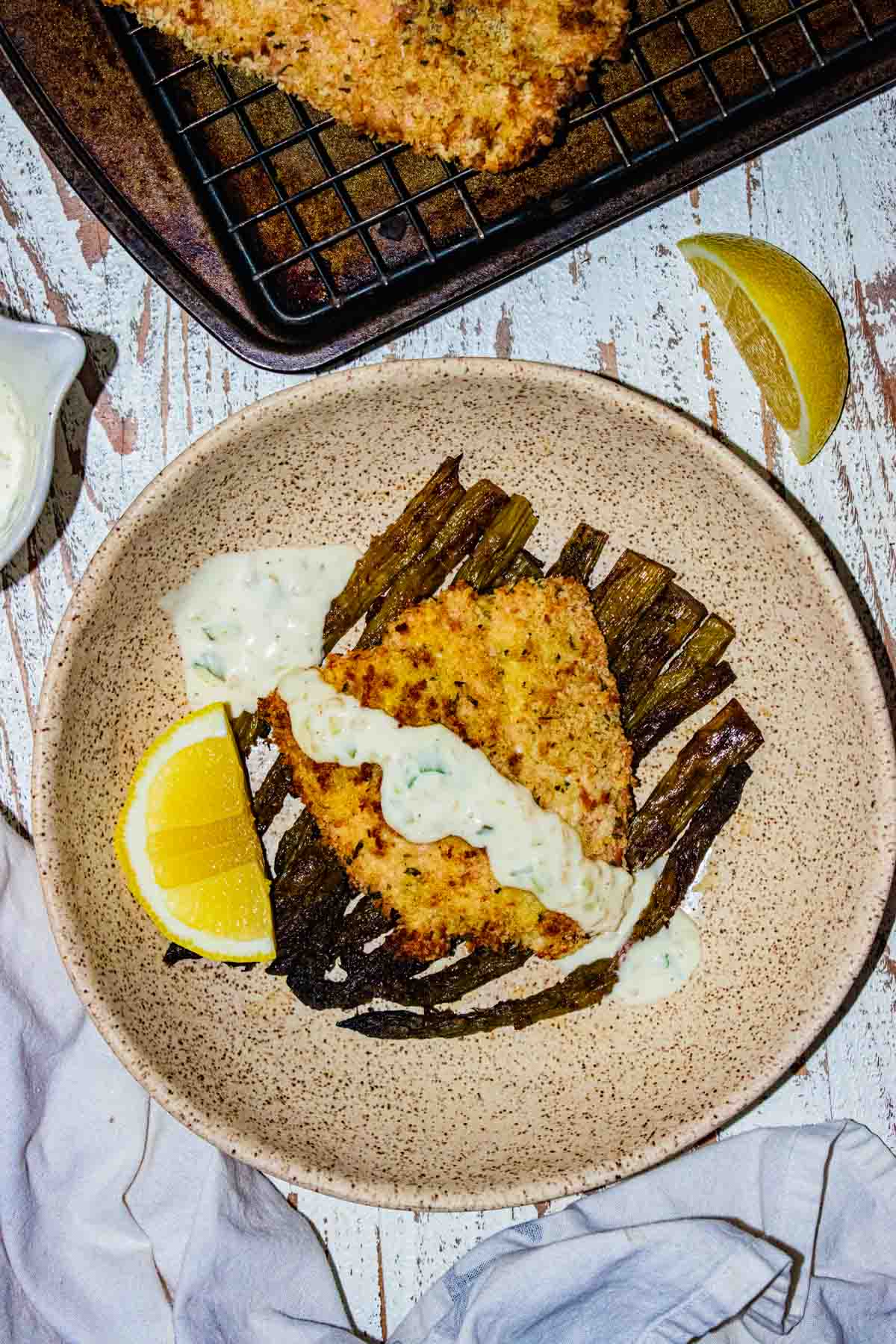 Birds-eye view of salmon on a cream colored plate with tartar sauce drizzled on top and a slice of lemon on the side.